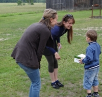 Kristīne Ģiga un Aina Budrēvica pasniedz jauno apavu pāri mazajam puikam Snēpelē